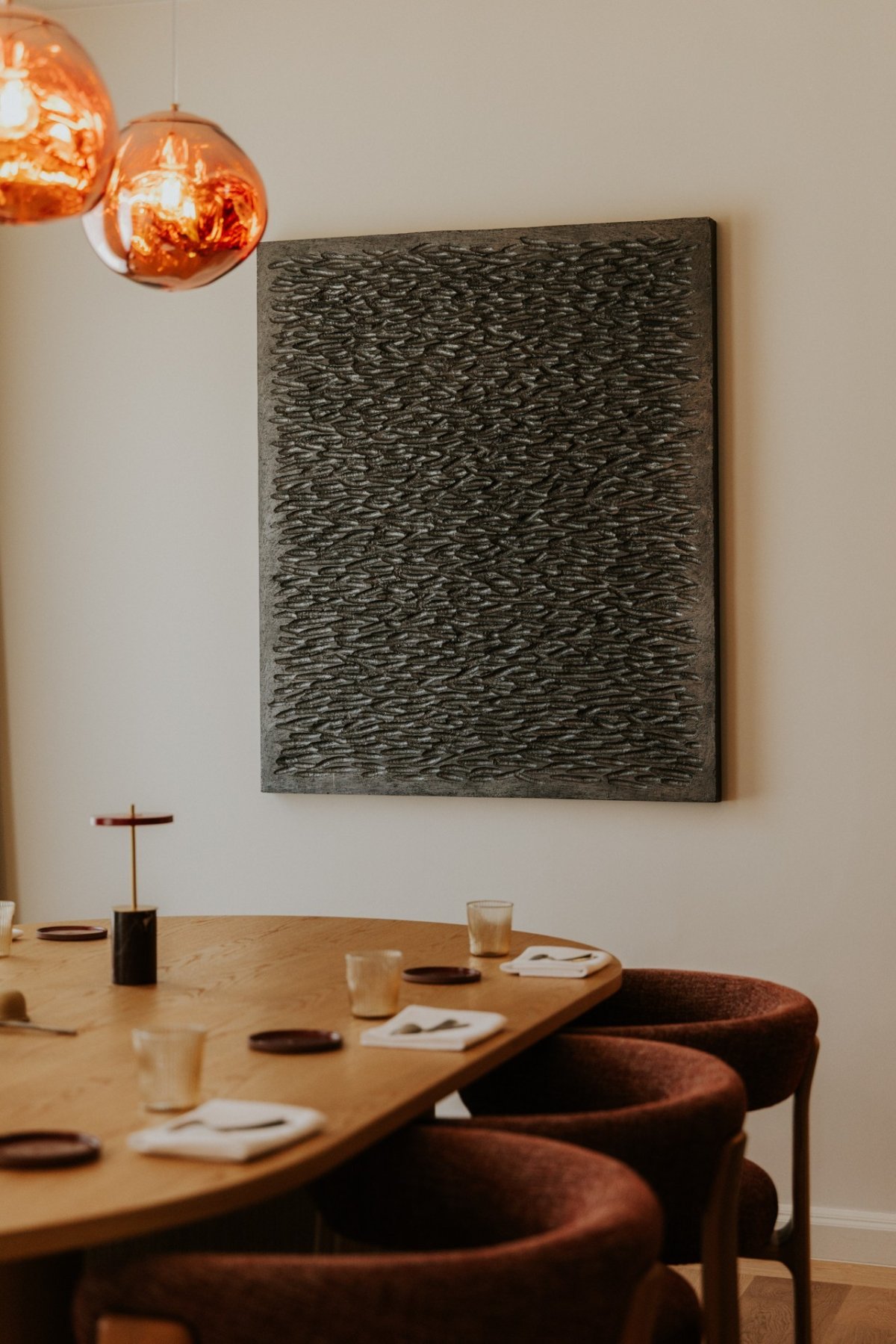 een gedekte, gezellige tafel met rode stoelen aan, uitkijkend op een diep zwart kunstwerk